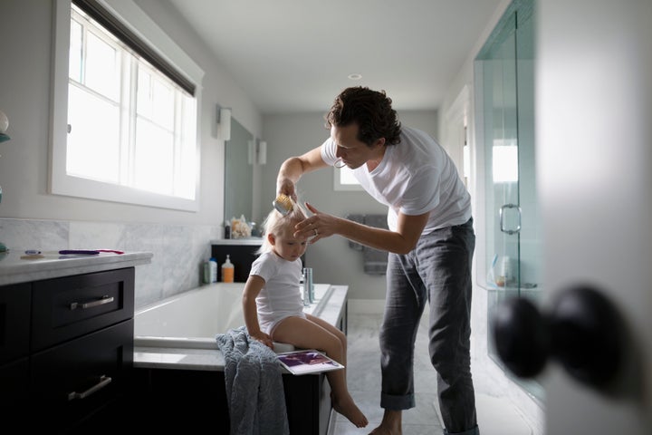 A man brushes a toddler's hair in a bathroom. 