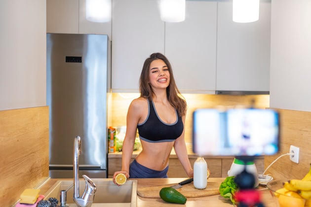 Young athletic girl is standing in the kitchen and is preparing a food. Young fit girl vlogging about healthy food. Fit healthy young girl recording her blog episode about healthy food diet