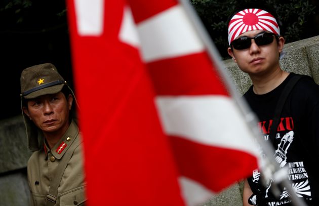 A man dressed as Japanese imperial army soldier and a man wearing a rising sun flag headband stand behind...