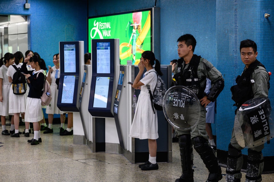Policemen in riot gear stand guard as a group of high school students gather inside the Kowloon Tong...