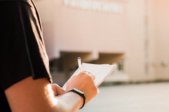 Young male person's hands holding a notepad and pen and writing information outdoors