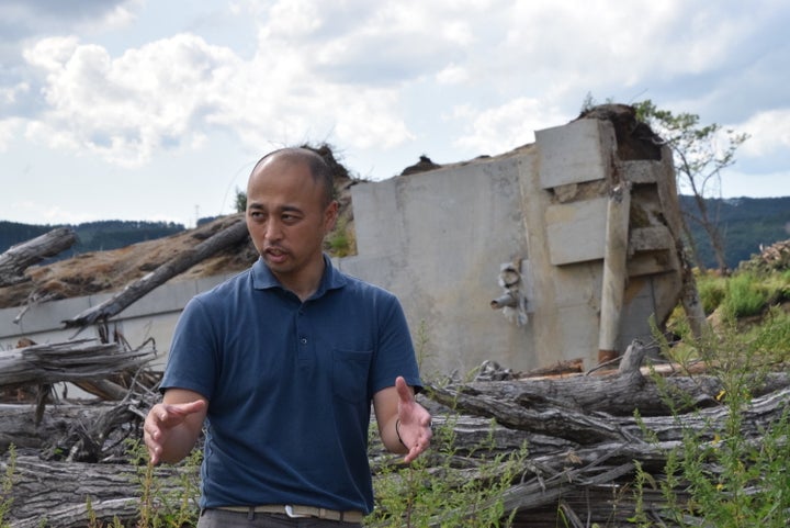 崩れた浄水場がある富里地区の説明をする宮久史さん。うしろには、杭ごと抜けて流された建物が残っている＝2019年9月1日