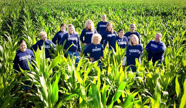 Dani Paluchniak (second from right) and employees in a cornfield. The riddle on the fronts and backs of their shirts is: “What did the baby corn say to the mama corn? Where’s pop corn?”