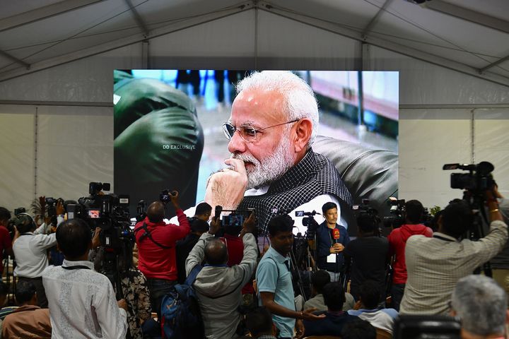 Members of the media cover the development as India's Prime Minister Narendra Modi is seen on a tv screen as he watches the live broadcast.