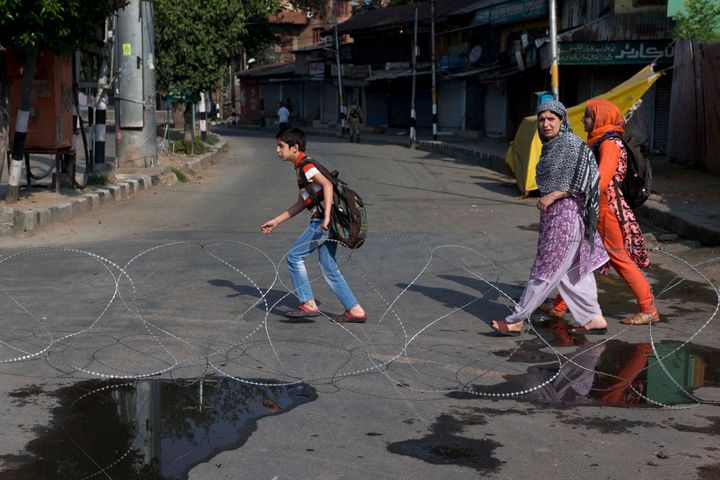 Kashmiri children accompanied by their mother walk past barbwire setup as road blockade by Indian paramilitary soldiers during lockdown in Srinagar, Indian controlled Kashmir, Friday, Aug. 23, 2019. The latest crackdown began just before Prime Minister Narendra Modi's Hindu nationalist-led government stripped Jammu and Kashmir of its semi-autonomy and its statehood, creating two federal territories. (AP Photo/Dar Yasin)