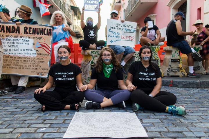 Three women sit with their mouths taped shut outside the government mansion La Fortaleza, where a small group of protesters gathered in San Juan, Puerto Rico, on Aug. 9, 2019. 