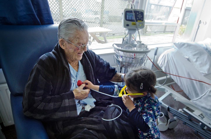 Small girl measuring heart beats to her sick grandfather with a toy stethoscope.