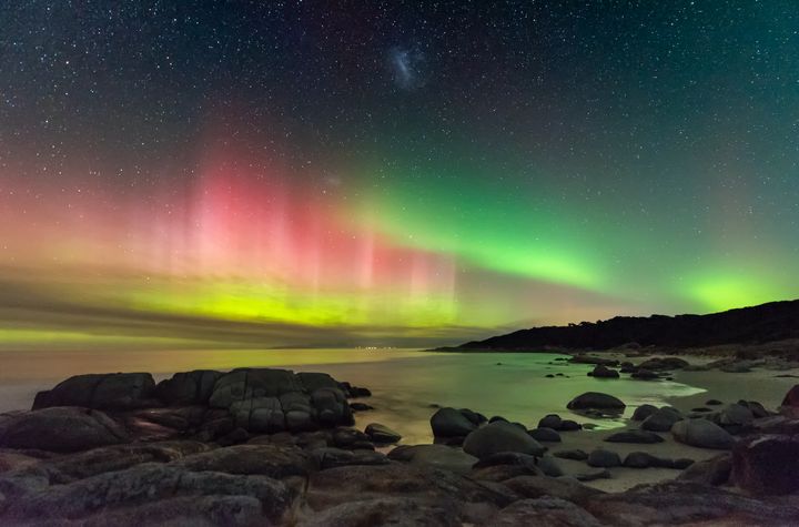 Aurora Australis from Beerbarrel Beach, by James Stone.A brightly coloured display of the Southern Lights beams high into the night sky on the east coast of Tasmania. The Large Magellanic Cloud also appears at the top centre of the image. Deserted beaches and minimal light pollution make Tasmania an ideal place to photograph the night sky, even more so when the aurora comes out to play.