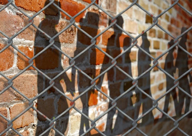 Shadows of people on a wall behind a fence