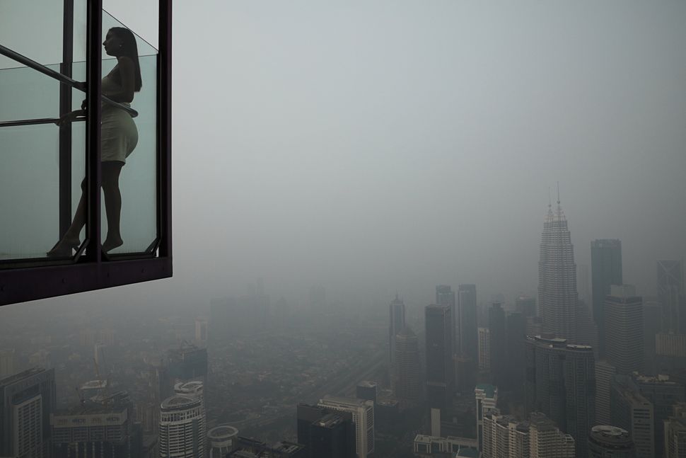 Ένας τουρίστας ποζάρει για μια φωτογραφία στον Πύργο της Κουάλα Λουμπούρ με φόντο τον ορίζοντα της πόλης που περιβάλλεται από ομίχλη, στην Κουάλα Λουμπούρ της Μαλαισίας στις 13 Σεπτεμβρίου.
