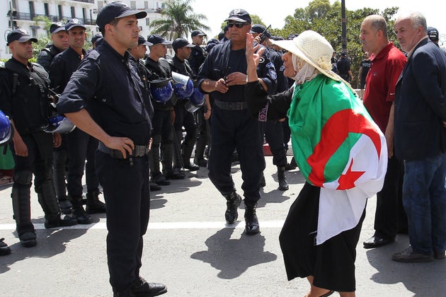 An Algerian protester wrapped with a national flag confronts riot police during the weekly Friday demonstration...