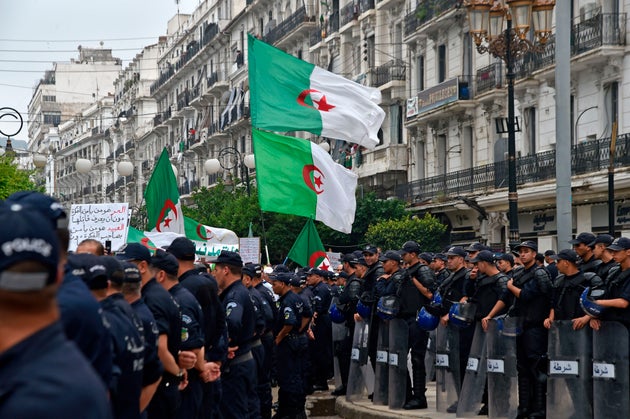 Algerian protesters wave their national flags next to security forces during a demonstration against...