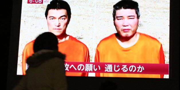A passer-by watches a TV news program reporting two Japanese hostages, Kenji Goto, left, and Haruna Yukawa,...
