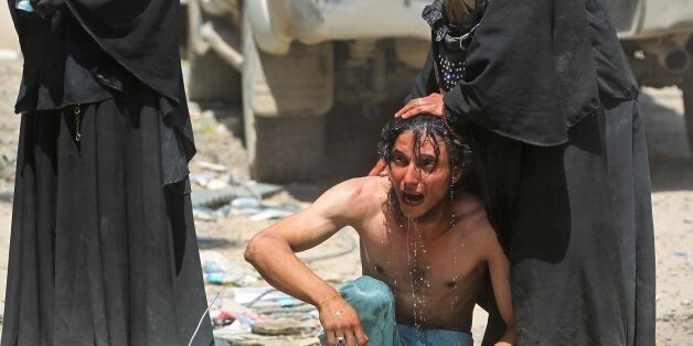 An Iraqi woman pours water to calm down a civilian, who witnessed a suicide attack as people were escaping the Old City of Mosul, as he cries on June 23, 2017.A suicide bomber blew himself up among civilians fleeing Mosul's Old City, where Iraqi forces are gaining ground against jihadists mounting a fierce but desperate defence, officers said. / AFP PHOTO / AHMAD AL-RUBAYE (Photo credit should read AHMAD AL-RUBAYE/AFP/Getty Images)