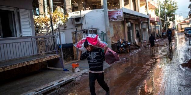 A boy carries clothes in a flooded street in the town of Mandra, northwest of Athens, on November 17, 2017.Six people were still missing in Greece on November 17, 2017 after a flash flood killed 16 others near the capital, with local communities facing food and medicine shortages and the full scope of the damage still unclear. / AFP PHOTO / Angelos Tzortzinis (Photo credit should read ANGELOS TZORTZINIS/AFP/Getty Images)