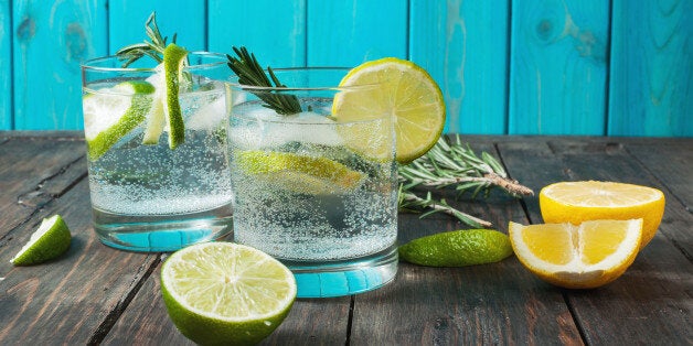 Alcoholic drink gin tonic cocktail with lemon, rosemary and ice on rustic wooden table