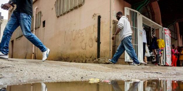 People pass a wall with graffiti as traders stand outside a shop on Robert Mugabe Street, on November 16, 2017 in Harare. Zimbabwe's President refused to immediately resign during talks on November 16 with generals who have taken control of Zimbabwe, a source close to the army leadership told AFP. / AFP PHOTO / - (Photo credit should read -/AFP/Getty Images)