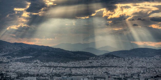 Dramatic sunset with rays of sunlight breaking through dramatic clouds over the city of Athens, Greece.
