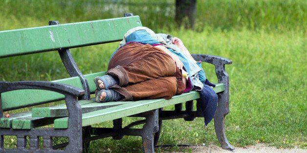 'Berlin, Germany - May 27, 2011: Homeless and old man sleeping on a bench near castle Charlottenburg in Berlin. Bench is in middle of avenue with pedestrian walkway. Man wears socks with holes so one can see his toes. His sandals are standing in front of bench.'