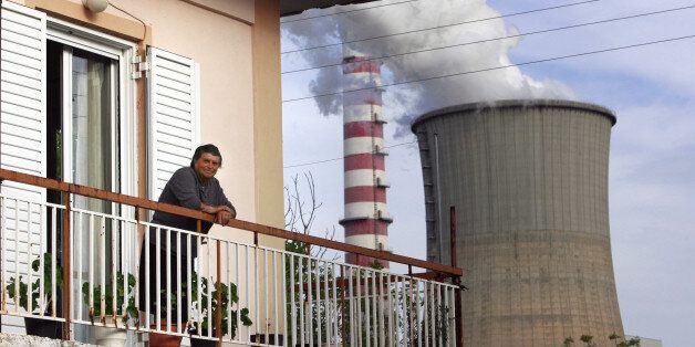 A woman stands on her balcony situated next to chimney stacks in the city of Megalopolis, about 120 km (75 miles) of Athens, May 15, 2009. The air in Greece's southern city of Megalopolis is heavy with dust and smoke spit by lignite plants, only about 100 metres from the nearest houses, but locals have blocked solar energy plans. Picture taken on May 15, 2009. To match feature GREECE-ENERGY/RENEWABLE/ REUTERS/John Kolesidis (GREECE ENVIRONMENT)