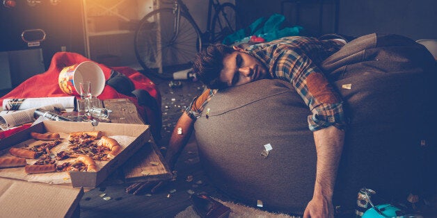 Young handsome man passed out on bean bag with joystick in his hand in messy room after party