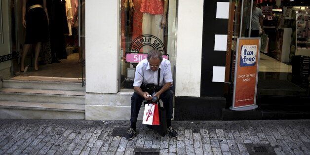 A man uses his mobile phone as he sits outside clothing store on a shopping street in downtown Athens, Greece August 28, 2015. Greece's economy grew 0.9 percent in the second quarter, compared with previous flash estimate of 0.8 percent earlier this month, helped by consumer spending and net exports, data showed on Friday. REUTERS/Stoyan Nenov
