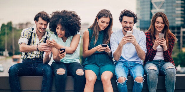 Multi-ethnic group of people sitting on an urban bridge text messaging and sharing smart phone content.