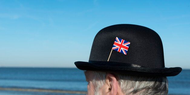 Englishman with bowler hat with union jack flag pinned on the hat on the beach overlooking the sea and towards Europe.