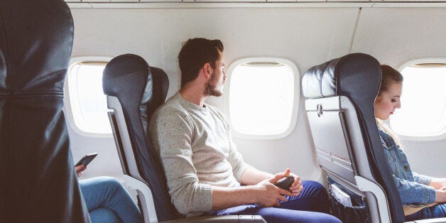 Young man sitting in airplane cabin near window. People flying by plane.