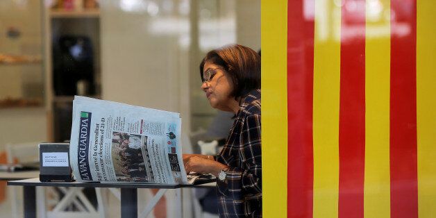 A woman reads a newspaper next to a Catalan flag at a coffee shop the day after the Catalan regional parliament declared independence from Spain in Barcelona, Spain, October 28, 2017. REUTERS/Jon Nazca