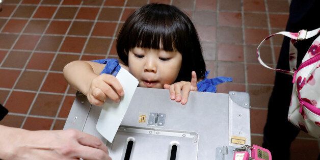 A girl casts her father's ballot for a national election at a polling station in Tokyo, Japan October 22, 2017. EUTERS/Kim Kyung-Hoon