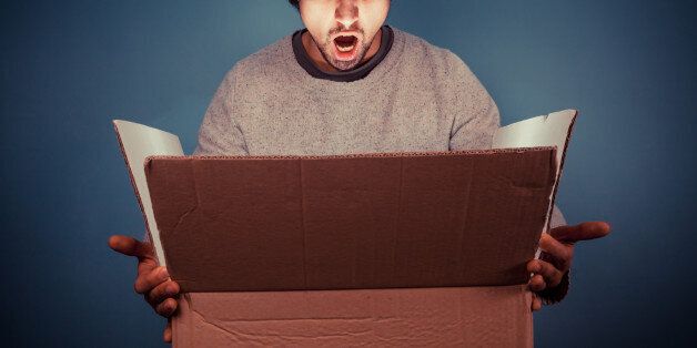 Surprised young man is opening a large cardboard box with something exciting inside it