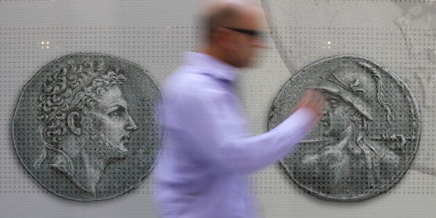 A man walks past pictures of ancient coins in central Athens, Greece, July 13, 2015. Euro zone leaders agreed on a roadmap to a possible third bailout for near-bankrupt Greece on Monday, but Athens must enact key reforms this week before they will start talks on a financial rescue to keep it in the European currency area. REUTERS/Jean-Paul Pelissier