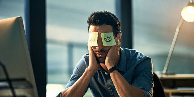 Shot of a tired young businessman working late in an office with adhesive notes covering his eyes