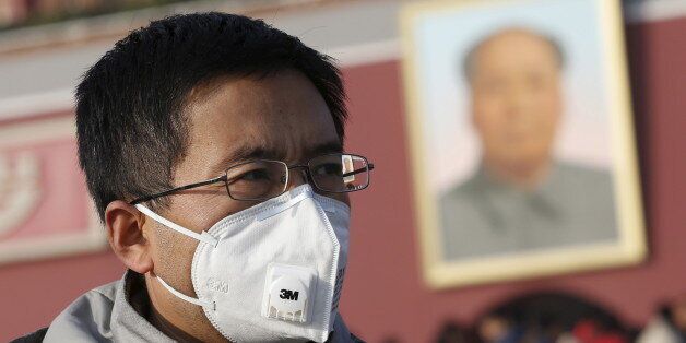 A man wearing a mask walks past the giant portrait of late Chinese chairman Mao Zedong at the Tiananmen Gate in Beijing, China, November 29, 2015. Beijing plans to ramp up its already tough car emission standards by 2017 in a bid by one of the world's most polluted cities to improve its often hazardous air quality. REUTERS/Kim Kyung-Hoon