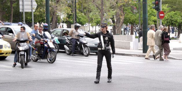 Athens, Greece - May 5th, 2005: A female traffic cop in Athens, Greece beckons oncoming traffic while stopped cars and other motorists wait their turn and pedestrians cross the street.