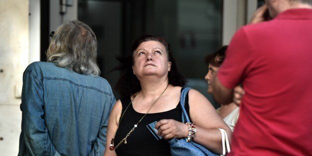 A woman holding a bank card looks up as people queue outside a bank to withdraw cash from an ATM in Athens on July 7, 2015. Eurozone leaders will hold an emergency summit in Brussels on July 7 to discuss the fallout from Greek voters' defiant 'No' to further austerity measures, with the country's Prime Minister Alexis Tsipras set to unveil new proposals for talks. European Commission head Jean-Claude Juncker said on July 7 that he was against an exit by Greece from the euro, even though Greeks massively rejected bailout terms in a referendum two days prior. AFP PHOTO / ARIS MESSINIS (Photo credit should read ARIS MESSINIS/AFP/Getty Images)