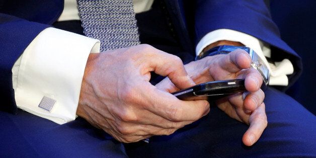 French Prime Minister Manuel Valls cheks his mobile phone as he attends the launching of a one-stop administrative point called