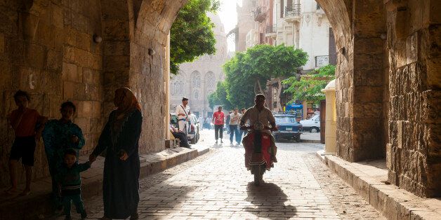 Cairo, Egypt - May 10, 2010: Pedestrians and a motorcyclist pass under an arched corridor on a street in Islamic Cairo, the architectural heart of medieval Cairo, Egypt.