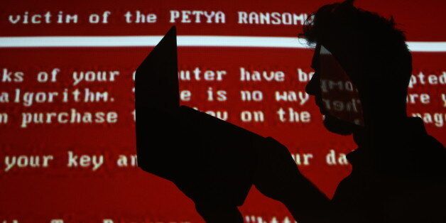 RYAZAN, RUSSIA - JUNE 28, 2017: A young man with a laptop computer against a red background with a projected message related to the Petya ransomware; on 27 June 2017 a variant of the Petya ransomware virus hit computers of companies in Russia, Ukraine, and other countries in a cyber attack. Alexander Ryumin/TASS (Photo by Alexander Ryumin\TASS via Getty Images)