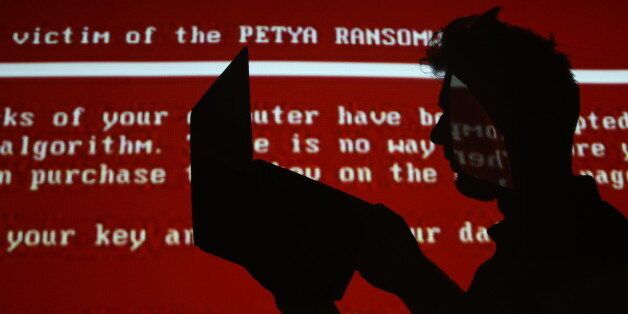 RYAZAN, RUSSIA - JUNE 28, 2017: A young man with a laptop computer against a red background with a projected message related to the Petya ransomware; on 27 June 2017 a variant of the Petya ransomware virus hit computers of companies in Russia, Ukraine, and other countries in a cyber attack. Alexander Ryumin/TASS (Photo by Alexander Ryumin\TASS via Getty Images)