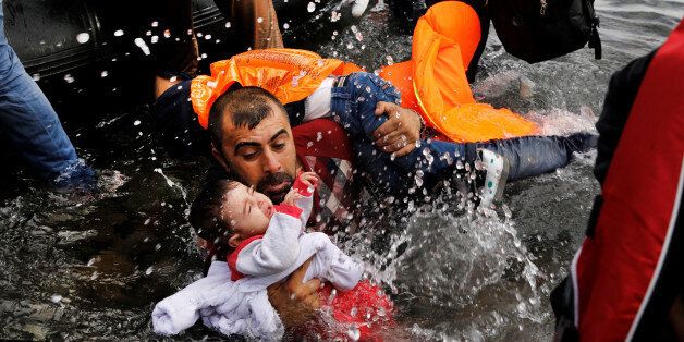 A Syrian refugee holds onto his two children as he struggles to disembark from a raft on the northern coast of the Greek island of Lesbos, after crossing a part of the Aegean Sea from Turkey to Lesbos September 24, 2015. Over 850,000 migrants and refugees have arrived on the Greek island in 2015. REUTERS/Yannis Behrakis