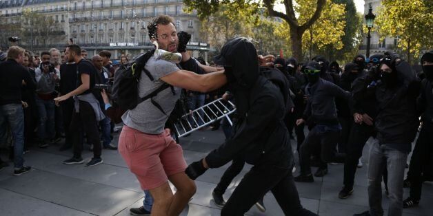 TOPSHOT - A demonstrator tries to prevent a group of balaclava-clad people from trying to take over a stage platform during a protest by La France Insoumise (LFI) leftist party parliamentary group over the French government's labour reforms on September 23, 2017 in Paris. Tens of thousands of French leftists are expected to answer a call by firebrand Jean-Luc Melenchon to throng the streets of Paris in protest over President Emmanuel Macron's sweeping reforms of the labour code. The third in a s