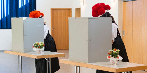 Women wearing traditional 'Bollenhut' pompon hats typical for the Black Forest region fill out their ballot papers at a polling station in Gutach near Freiburg, southwestern Germany, during general elections on September 24, 2017.Polls opened in Germany in a general election expected to hand Chancellor Angela Merkel a fourth term, while the hard-right Alternative for Germany (AfD) party is predicted to win its first seats in the national parliament. / AFP PHOTO / THOMAS KIENZLE (Photo credit should read THOMAS KIENZLE/AFP/Getty Images)