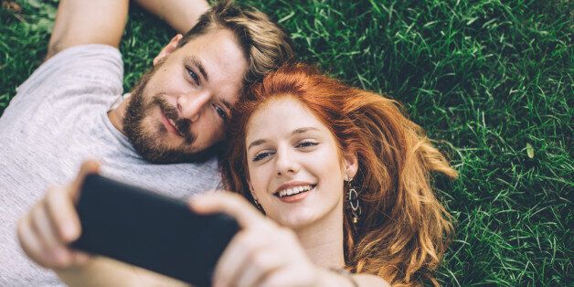Young couple laying on green grass . Taking selfie with smart phone. They are happy and joyful. Enjoying in summer day.