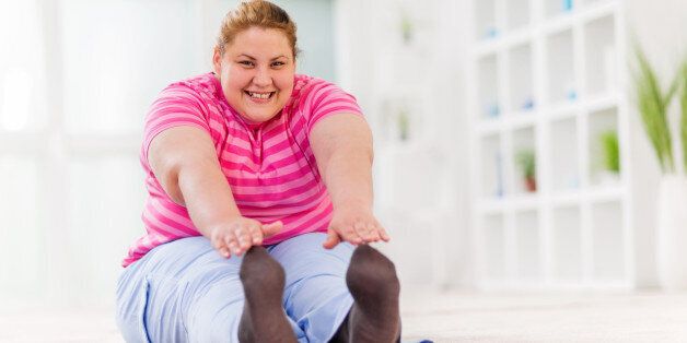 Young overweight smiling woman sitting on the floor and stretching while looking at camera.