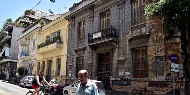 People pass a neoclassical building for sale in one of the oldest districts of Athens on July 7, 2017.A 1983 law for the conservation and development of neoclassical buildings obliged the property owners to restore them, but the 2010 crisis, the over-taxation of real estate and the absence of loans or State aid has led lead to their abandonment. 'Currently, with the crisis, it is expensive and difficult to repair this kind of buildings, there are no more state aids, people prefer to abandon or demolish them,' says architect Maria Daniil , specialized in the buildings of the end of the nineteenth and twentieth centuries.Famous for its ancient sites, Athens also has a neoclassical architectural heritage of the nineteenth and twentieth centuries, of which the few remaining buildings are threatened with disappearing for lack of a policy in favor of their conservation. / AFP PHOTO / LOUISA GOULIAMAKI (Photo credit should read LOUISA GOULIAMAKI/AFP/Getty Images)