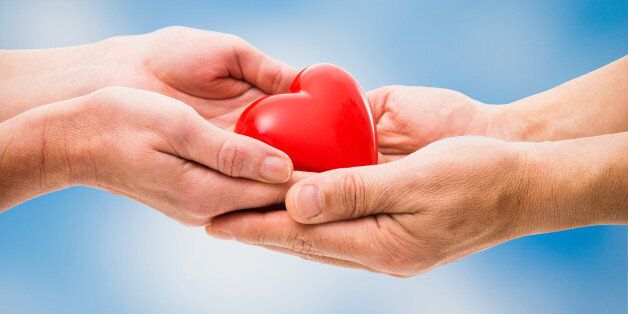 Red heart in human hands on blue sky background