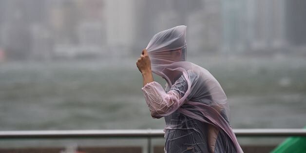 A man shields himself with his plastic poncho during heavy winds and rain brought on by Typhoon Hato in Hong Kong on August 23, 2017.Typhoon Hato smashed into Hong Kong on August 23 with hurricane force winds and heavy rains in the worst storm the city has seen for five years, shutting down the stock market and forcing the cancellation of hundreds of flights. / AFP PHOTO / Anthony WALLACE (Photo credit should read ANTHONY WALLACE/AFP/Getty Images)