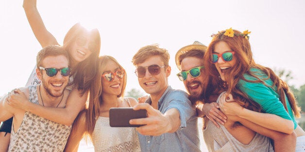 Group of young people on the beach having party. Taking selfie and dancing. They are happy and joyful. Sunny day.